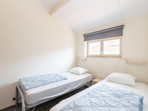 A small, clean room with two single beds, a window with a view, and a bedside table. - Holiday Home in Koksijde Near Sint-andre Beach (Koksijde)