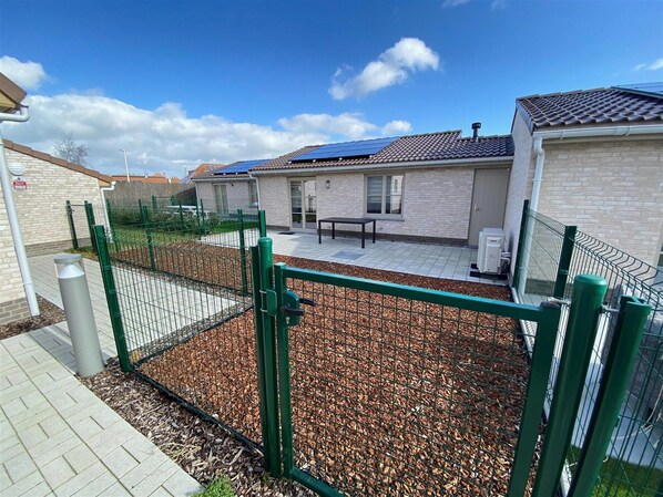 A fenced outdoor area with a patio, a bench, and a building with a tiled roof. - Holiday Home in Koksijde Near Sint-andre Beach (Koksijde)