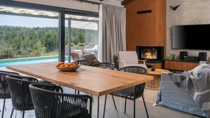Una sala moderna con una mesa de comedor de madera, sillas de mimbre negro, un televisor de pantalla plana montado en la pared y una chimenea.
