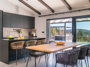 A modern kitchen with dark cabinetry, a central island, and a dining area with wicker chairs. - Villa Noeli With Swimming Pool (Buzet)