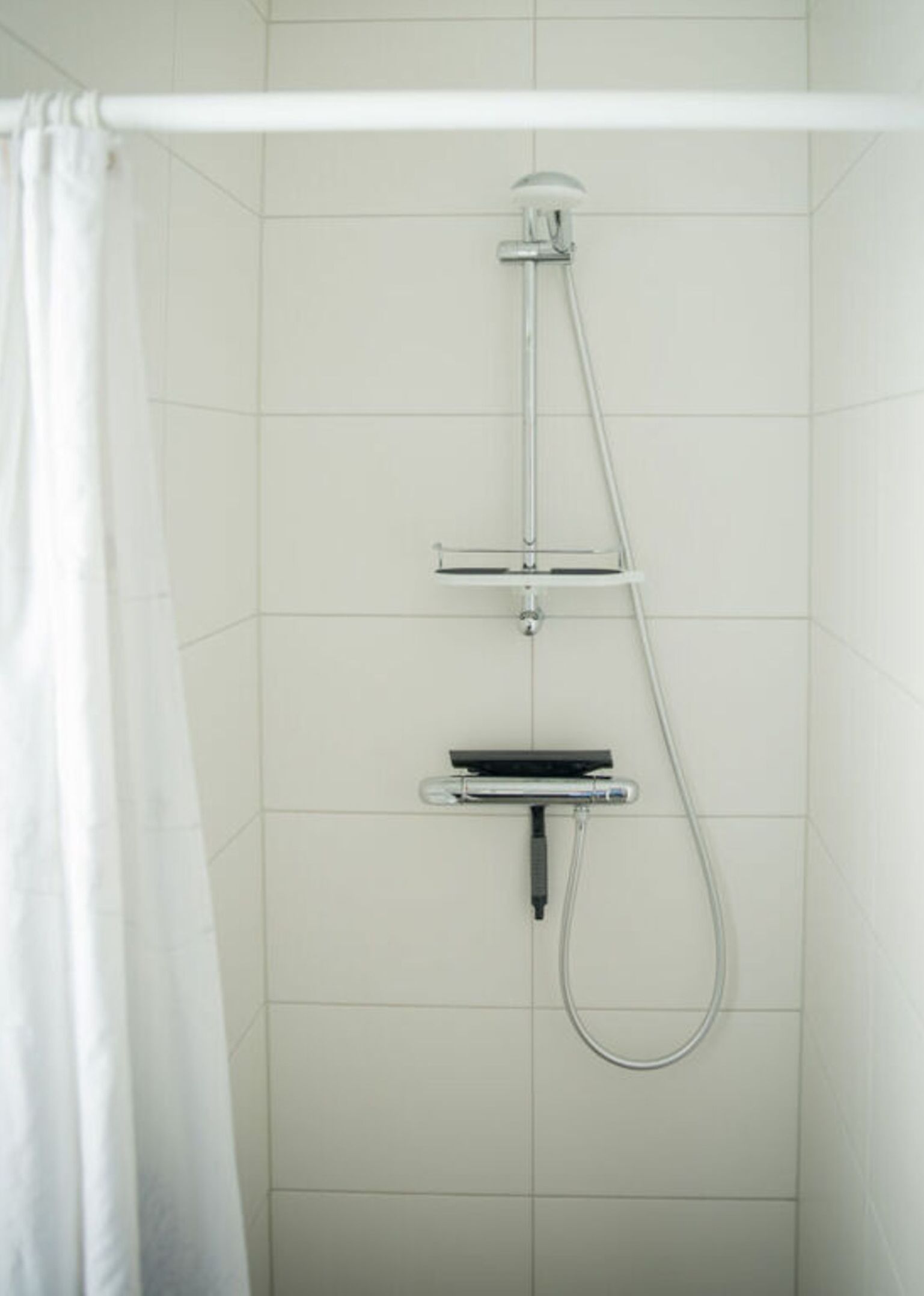 A shower with a handheld showerhead, a handheld scrubber, and a wall-mounted control panel.