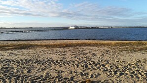 A sandy beach with a pier extending into the water, a clear sky, and a distant building. - Jessen Modern Retreat (Gelting)