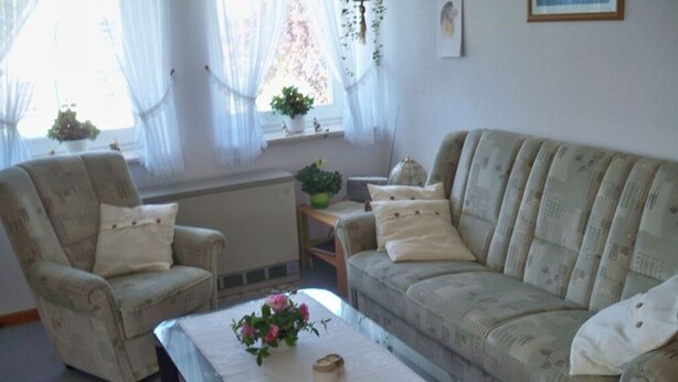 A living room with a sofa, armchair, and a glass coffee table with a vase of flowers. - Jessen Modern Retreat (Gelting)
