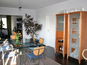 Ein moderner Essbereich mit einem Glastisch, Stühlen, einer Topfpflanze und einem Weinkühlschrank.