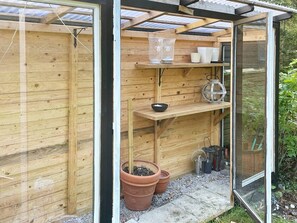 Una estructura de madera con puerta de vidrio, estantes con vajilla y plantas en macetas.