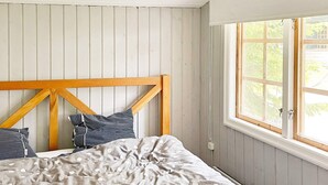 A bedroom with a wooden headboard, a bed with a patterned bedspread, and a window with a view of greenery. - 5 Person Holiday Home in Djurhamn-by Traum (Djurhamn)