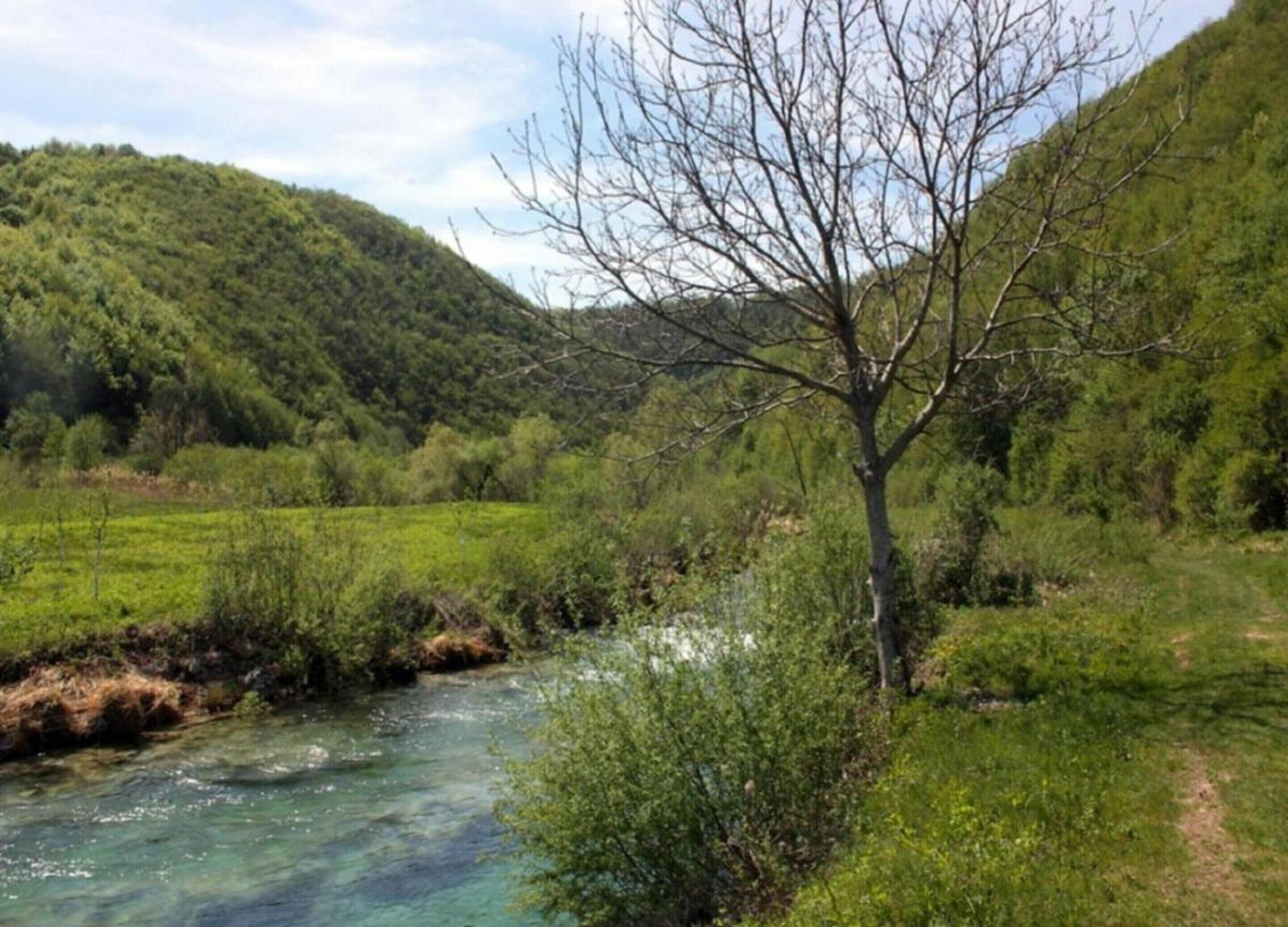 A river flowing through a lush green valley with a hill in the background.