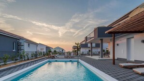 A swimming pool with lounge chairs, a covered patio area, and modern buildings in the background. - Comfort Villa With Swimming Pool and Terrace (Sukosan)