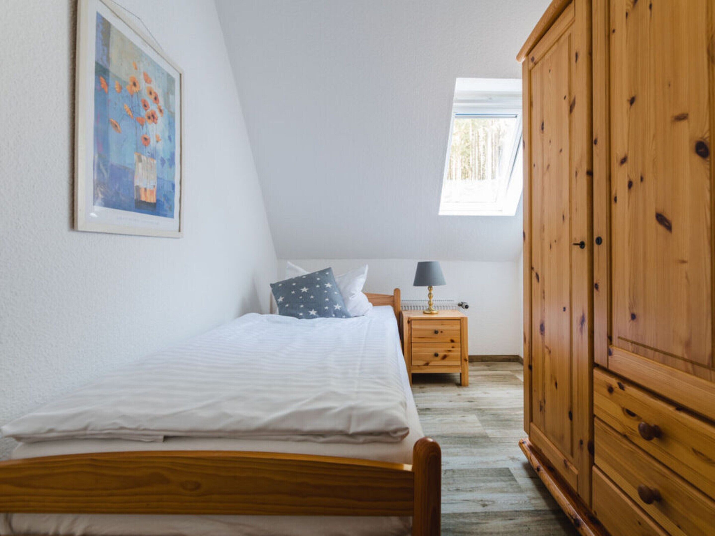 A bedroom with a bed, a nightstand, a lamp, a wardrobe, and a painting on the wall.