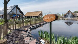 Ein hölzernes Schild mit der Aufschrift 'Lagodi di Vin', ein Teich mit einer Fontäne, ein Steinweg und Gebäude mit Strohdächern.