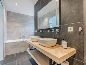 Une salle de bain moderne avec deux grands lavabos sur pied, une baignoire et un grand miroir au-dessus des lavabos.