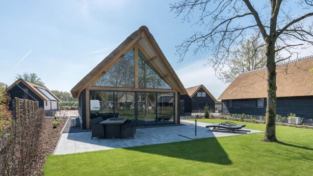 Ein modernes Haus mit einem großen Panoramafenster, einem Reetdach und einem gepflegten Rasen.