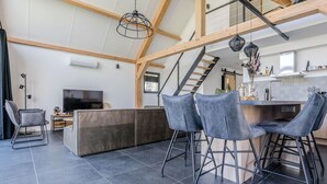 Eine moderne Küche mit Barbereich, einem Essbereich mit Barhocker, einem Fernseher und einer Treppe zu einer oberen Ebene.