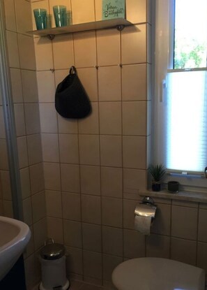 Un baño con inodoro, lavabo y estante con vasos verdes.