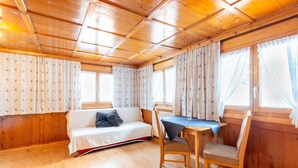 Une pièce chaleureuse avec un plafond en bois, un canapé agrémenté d’un coussin, une table recouverte d’une nappe bleue et deux chaises.