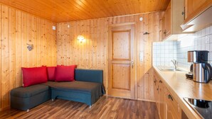 L’intérieur d’un chalet en bois, avec un canapé, un coin cuisine et une porte.
