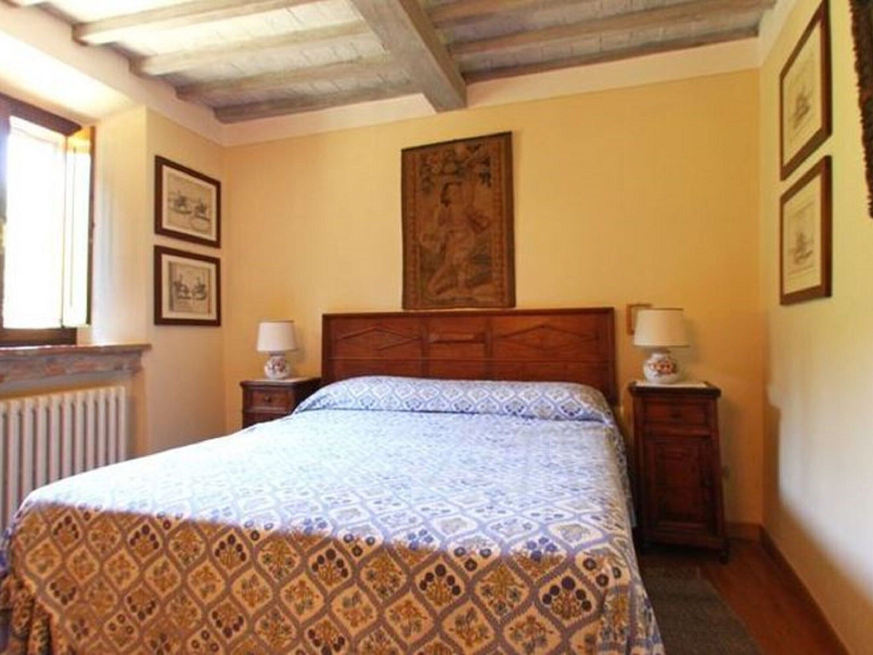 A bedroom with a wooden headboard, a patterned bedspread, two bedside tables with lamps, and framed pictures on the walls.