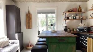 Een keuken met een centraal kookeiland, barkrukken, een magnetron en een koffieapparaat.