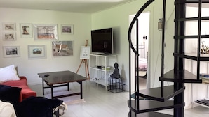 Een woonkamer met een wenteltrap, een bank, een tafel, een televisie en kunstwerken aan de muren.