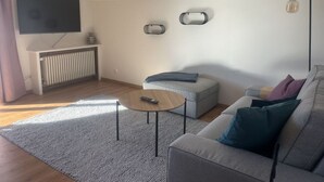 A modern living room with a grey sofa, a small round coffee table, a grey armchair, and a television on a stand. - 1 Porzig Modern Retreat (Fischen im Allgaeu)