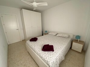 Quarto com cama, guarda-roupa, ventoinha no teto e mesas de cabeceira.
