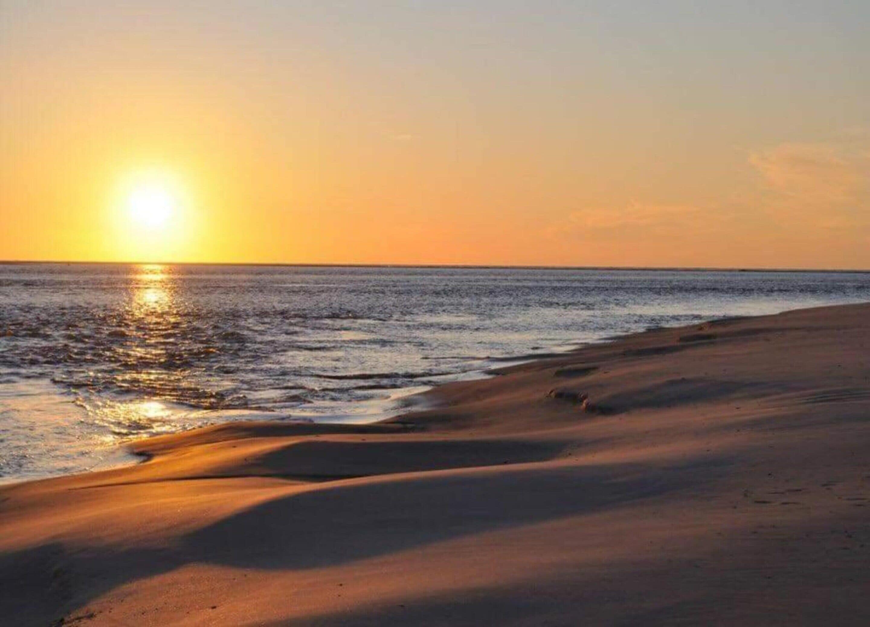 Ein Strand bei Sonnenuntergang, wobei sich die Sonne im Wasser spiegelt.