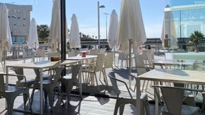 Un espace de restauration en plein air avec des tables et des chaises, des parasols et une vue sur un bâtiment moderne et des palmiers.