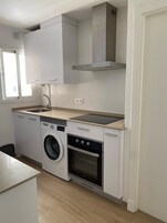 Une cuisine compacte équipée d’un lave-linge, d’un four et d’une plaque de cuisson intégrée.