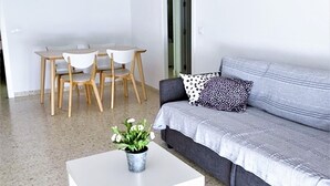 Un salon moderne avec un canapé gris, une table basse blanche agrémentée d’une plante, et un coin repas avec des chaises et une table en bois.