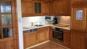 A kitchen with wooden cabinets, a microwave, a sink, a dishwasher, and an oven. - Blauort in Friedrichskoog-spitze (Friedrichskoog)
