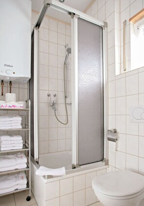 Bathroom features a walk-in shower with a frosted glass door, a toilet, and a shelf with towels.