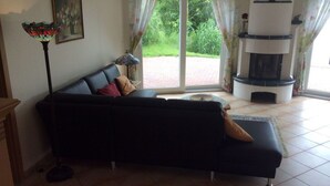 Un salon avec un canapé noir, un lampadaire, une cheminée et une vue sur la verdure à l’extérieur.
