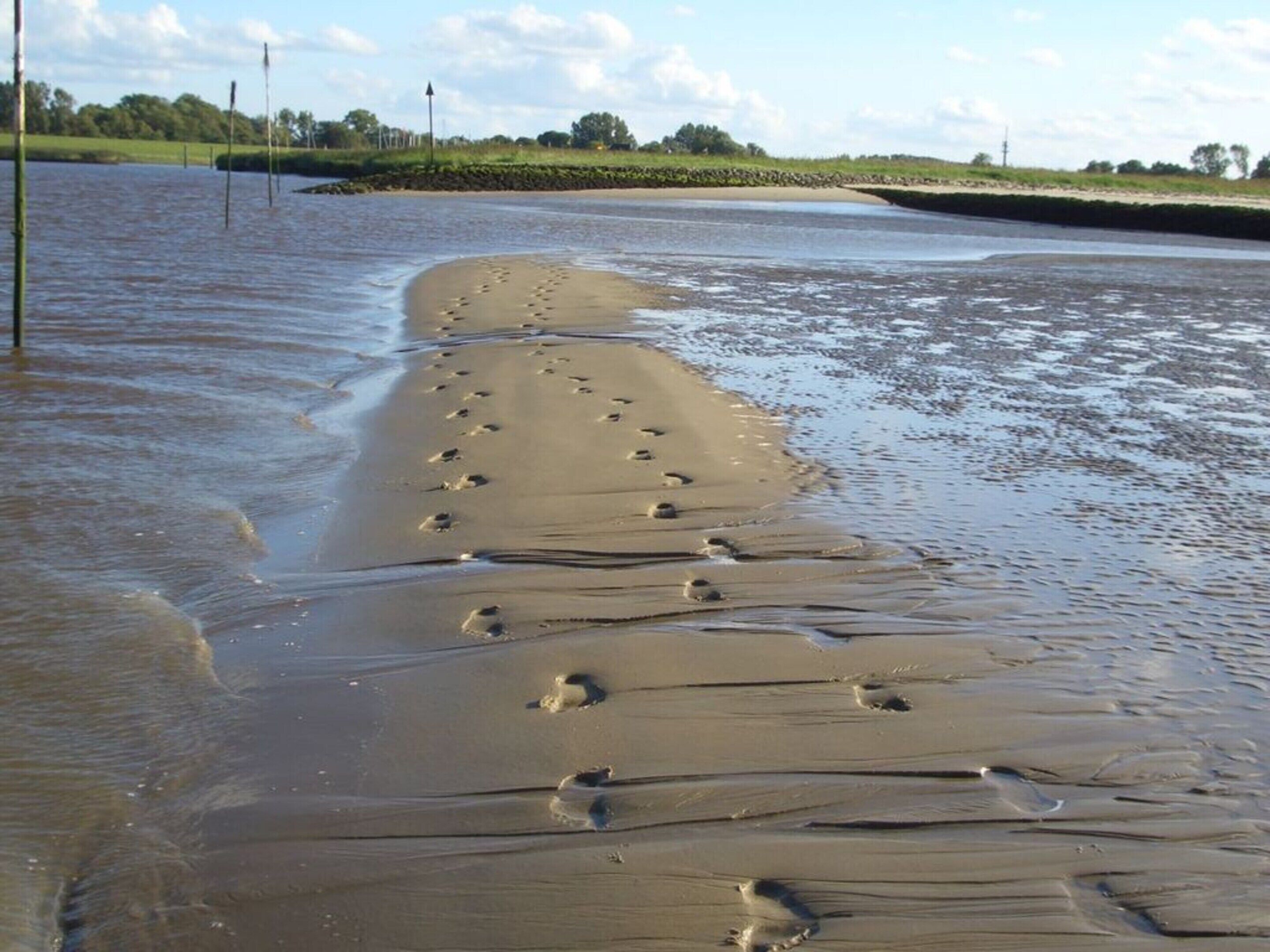 Uma praia arenosa com pegadas que se estendem até a água.