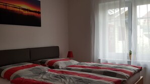 Makuuhuone, jossa on sänky, yöpöytä, lamppu ja ikkuna, jossa on ohuet verhot.