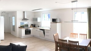 Une cuisine moderne avec des meubles blancs, un four à micro-ondes et une cuisinière. On y trouve également un coin repas avec une table et des chaises.