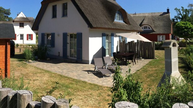 Une maison blanche avec un toit de chaume, un patio avec des meubles d’extérieur et un monument en pierre au premier plan.