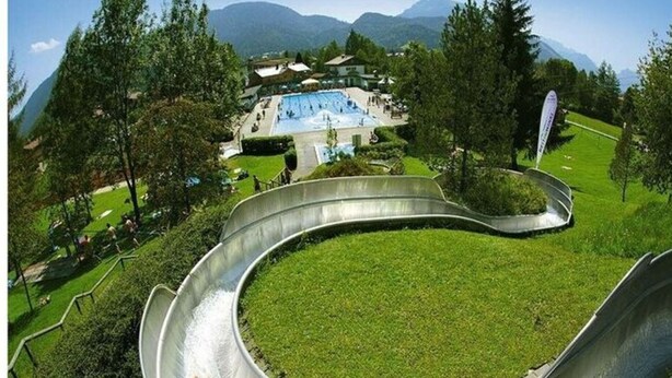 A water slide with a pool at the bottom, surrounded by greenery and a mountainous backdrop. - Holiday Apartment Dosbach (Reit im Winkl)