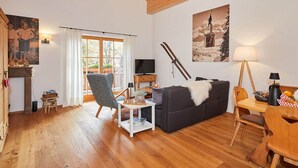 A cozy living room with wooden floors, a dark sofa, a small table, a TV, and a painting of a mountain scene. - Holiday Apartment Dosbach (Reit im Winkl)