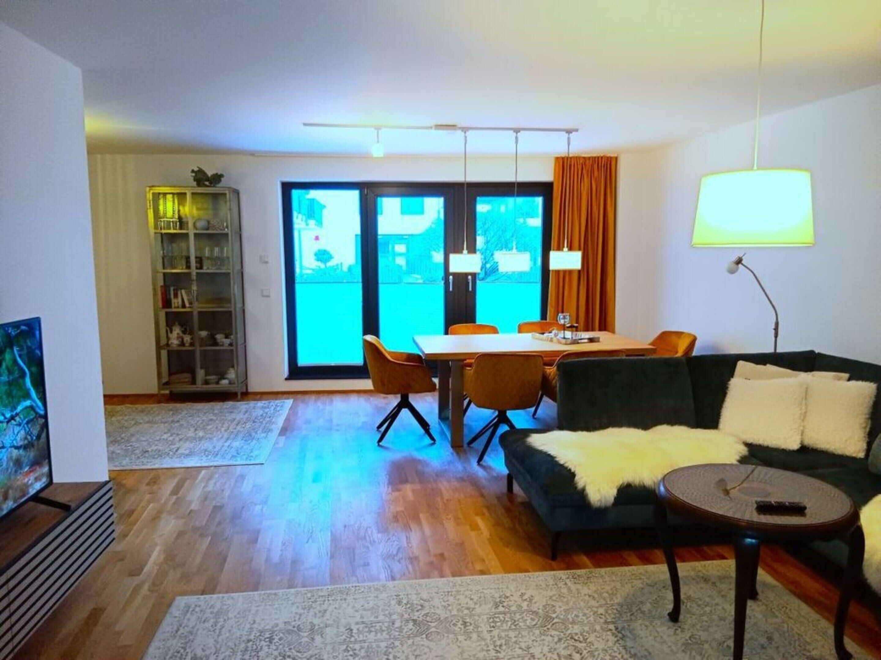 A modern living room with a sofa, coffee table, and a dining area with chairs and a table.