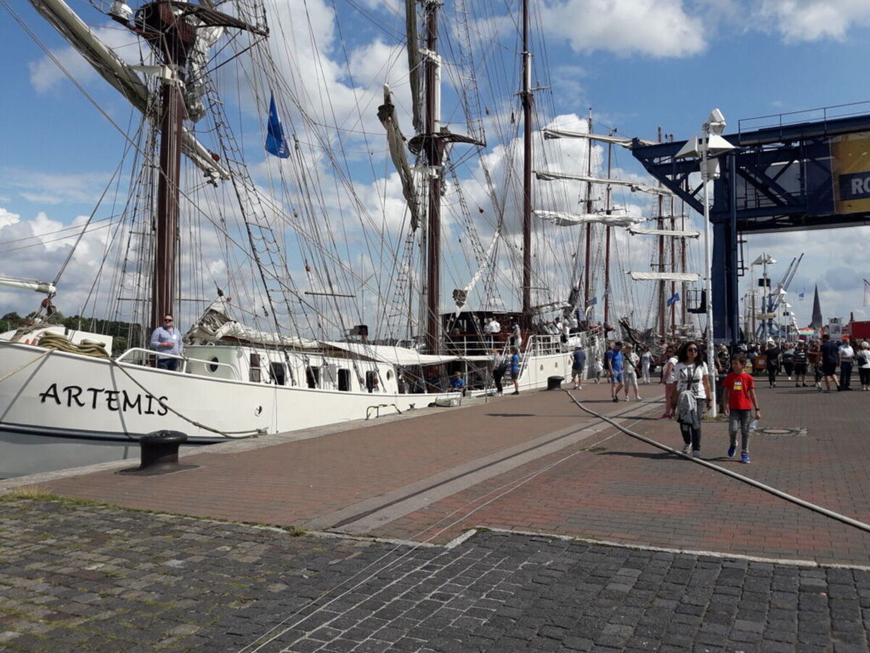 Eine Uferpromenade, an der ein weißes Boot namens 'ARTEMIS' liegt.