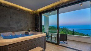 Une salle de bain moderne avec une grande baignoire, une petite table avec une chaise et un balcon offrant une vue sur la mer.