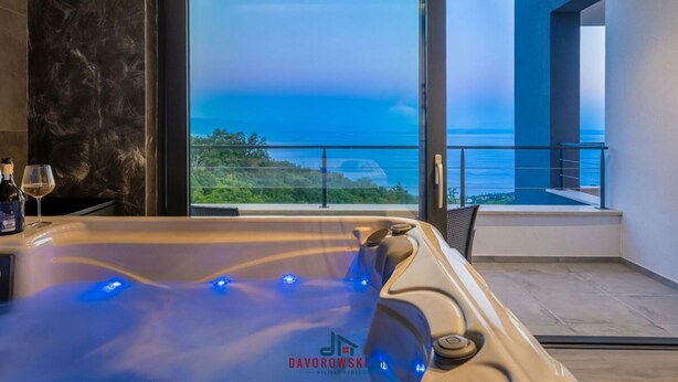 Une salle de bain moderne dotée d’un jacuzzi et d’une porte vitrée donnant sur un balcon avec vue sur la mer.