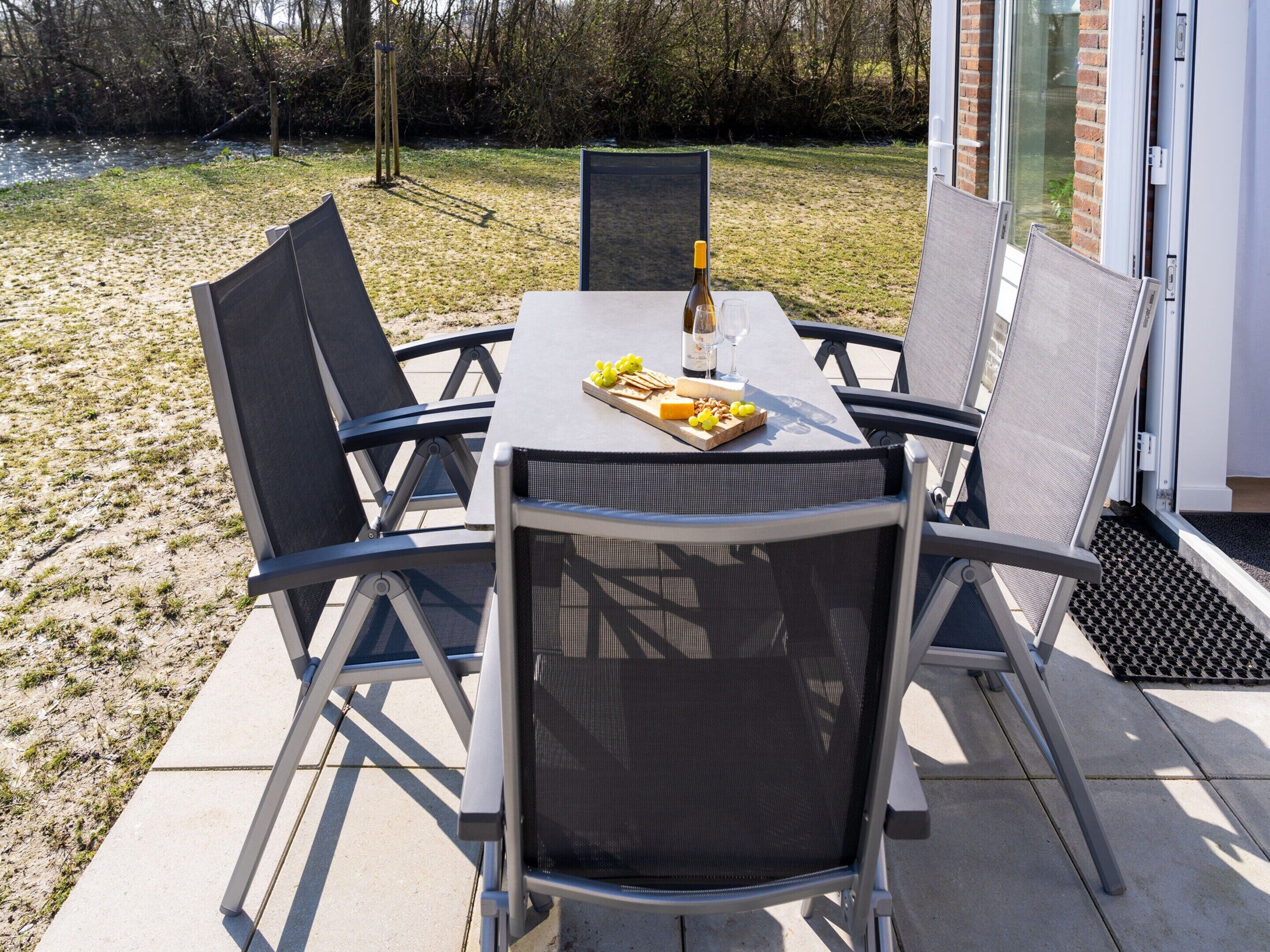 Une terrasse extérieure avec une table dressée pour deux personnes, agrémentée d’une bouteille de vin, de verres et d’une planche de fromages.