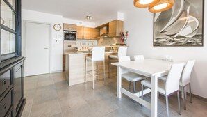 A modern kitchen with white cabinetry, a central island, and a dining area with a white table and chairs. - Beautiful Apartment on the sea Wall (Blankenberge)