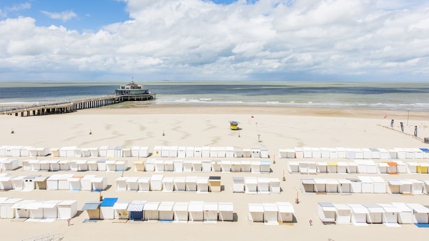 A beach with rows of white beach huts, a pier, and a lifeguard tower. - Beautiful Apartment on the sea Wall (Blankenberge)