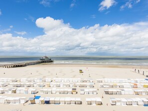 A beach with rows of white beach huts, a pier, and a lifeguard tower. - Beautiful Apartment on the sea Wall (Blankenberge)