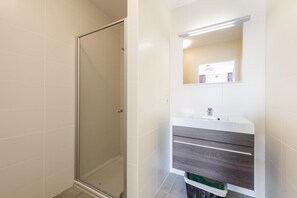 Une salle de bain avec une douche à parois de verre, un lavabo blanc et un miroir au-dessus du meuble-lavabo.
