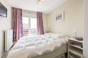 Une chambre d’hôtel avec un lit, une table de chevet, une lampe, un tableau encadré au mur et une fenêtre avec des rideaux.
