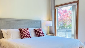A neatly made bed with white and red patterned pillows, a wooden headboard, and a nightstand with a lamp.