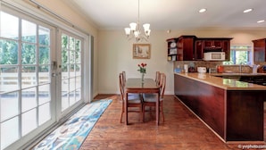 A spacious kitchen with a large island, a dining area with a table and chairs, and a view through the glass doors.